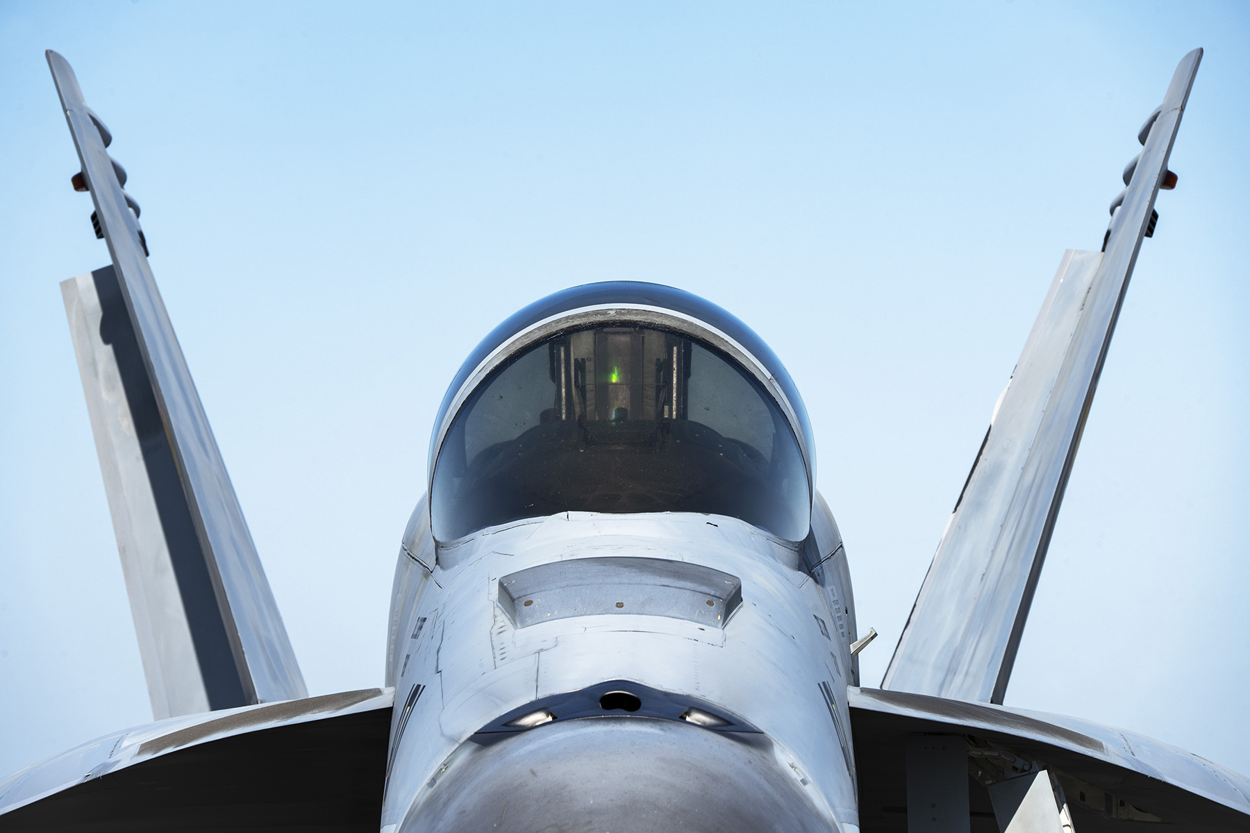 Primer plano de la cabina y el elegante diseño de un moderno avión de combate en tierra bajo un cielo azul despejado.