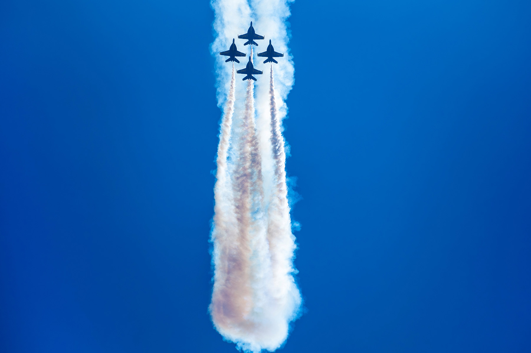Cuatro cazas en formación cerrada dejan espectaculares estelas de vapor sobre un cielo azul vibrante, mostrando técnicas fotográficas expertas en espectáculos aéreos.