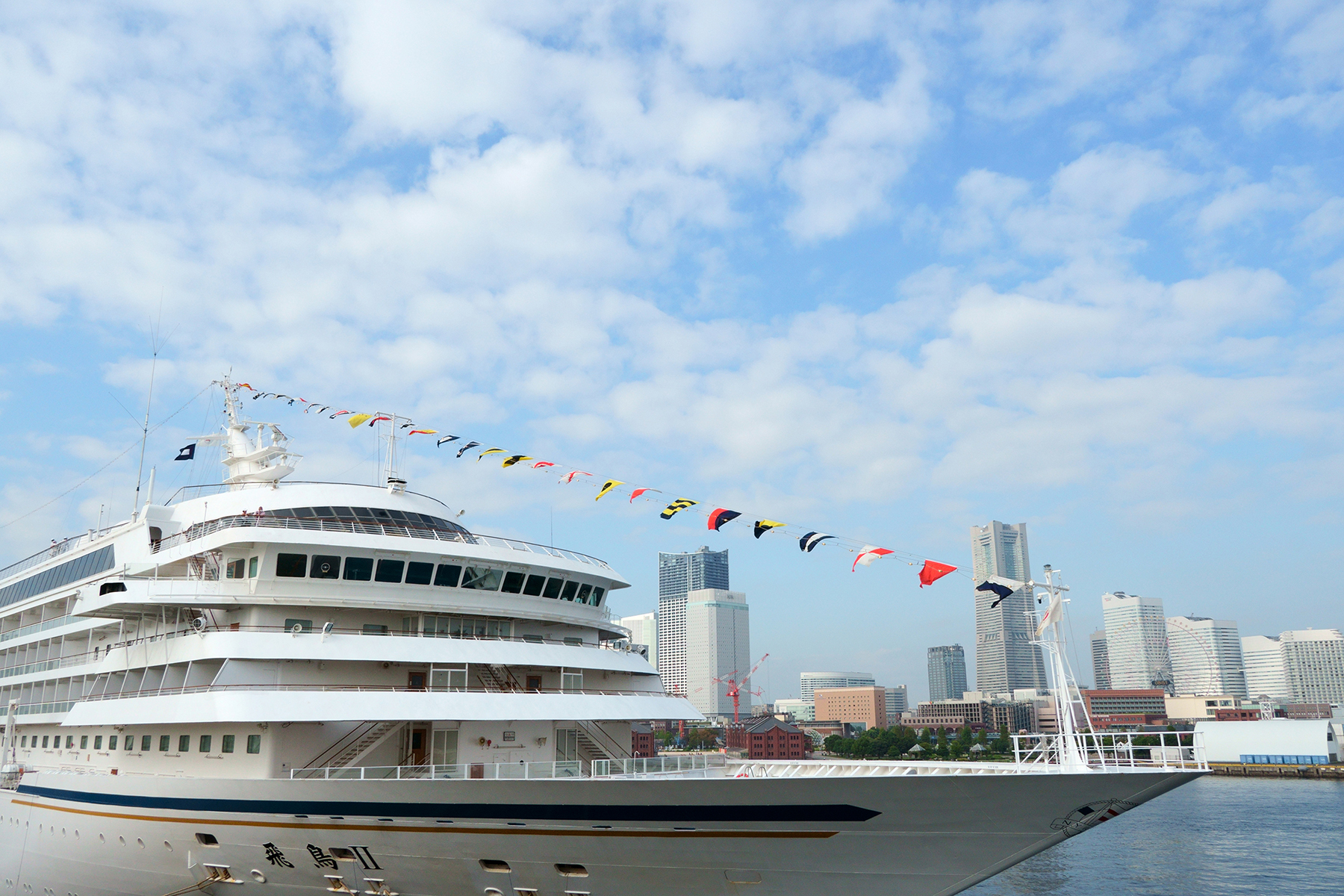 A luxurious cruise ship adorned with colorful flags docked near a city skyline under a bright, blue sky.