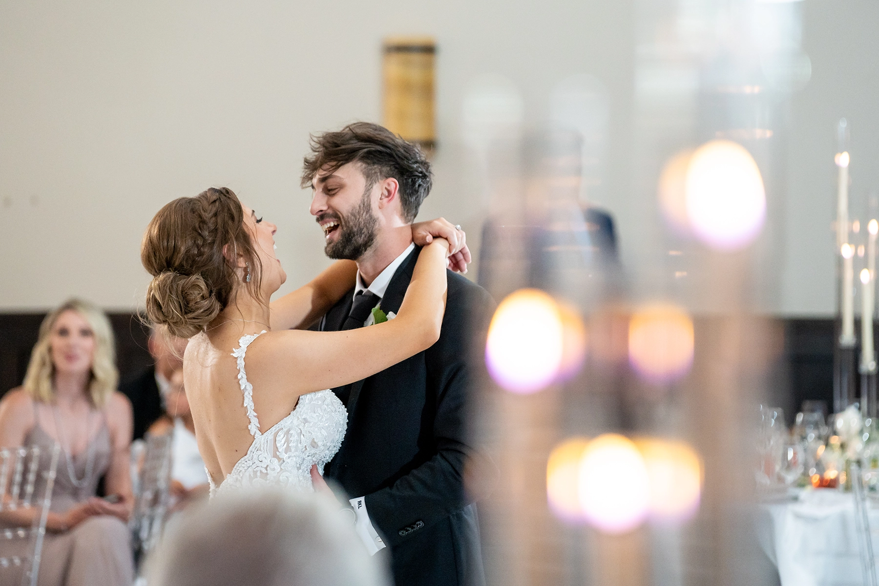 Bride and groom share their first dance, beautifully captured in documentary style wedding photography with warm candlelight and a blurred romantic ambiance.