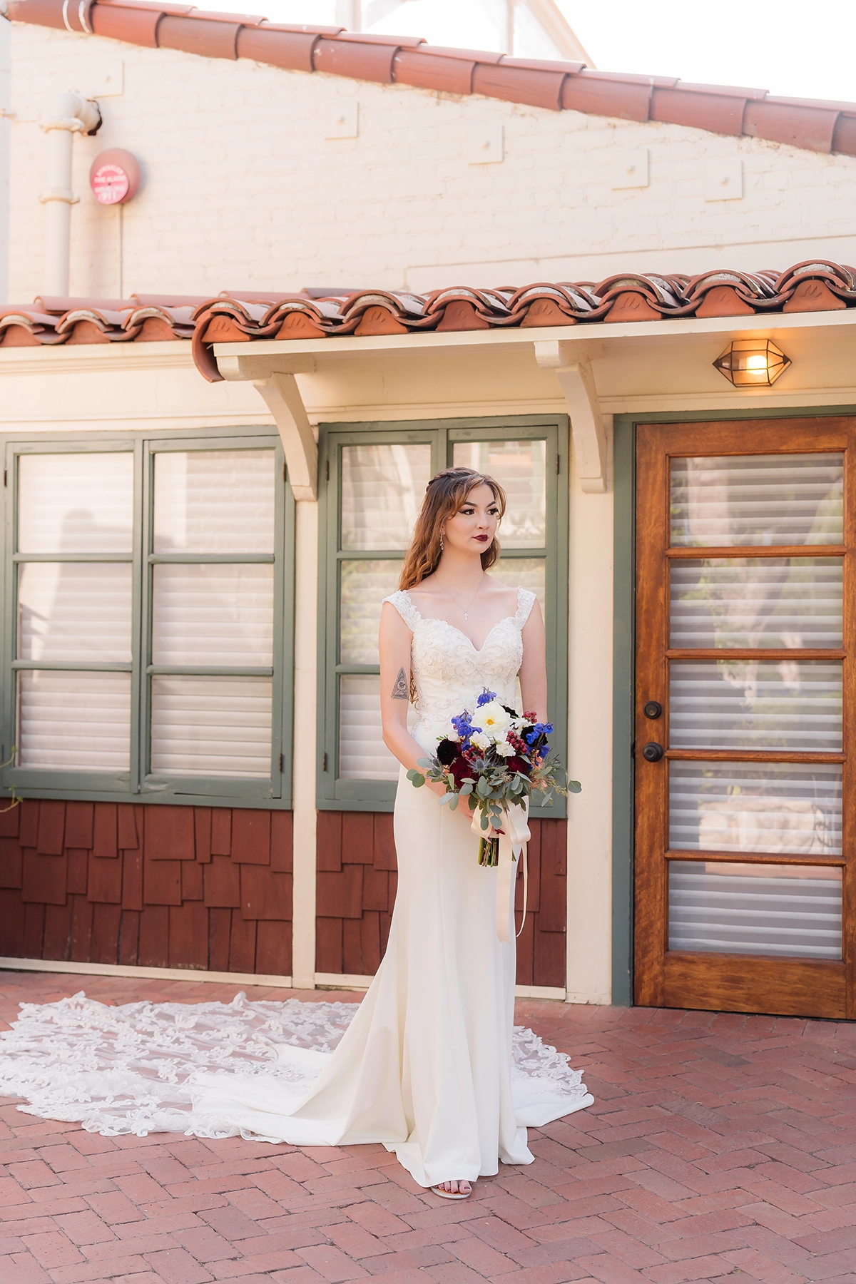 Una novia con un elegante y moderno vestido de novia frente a una casa de campo rústica, sosteniendo un ramo de flores vibrantes, mostrando la tendencia de fotografía de boda 2025 de mezclar el encanto vintage con la elegancia contemporánea.