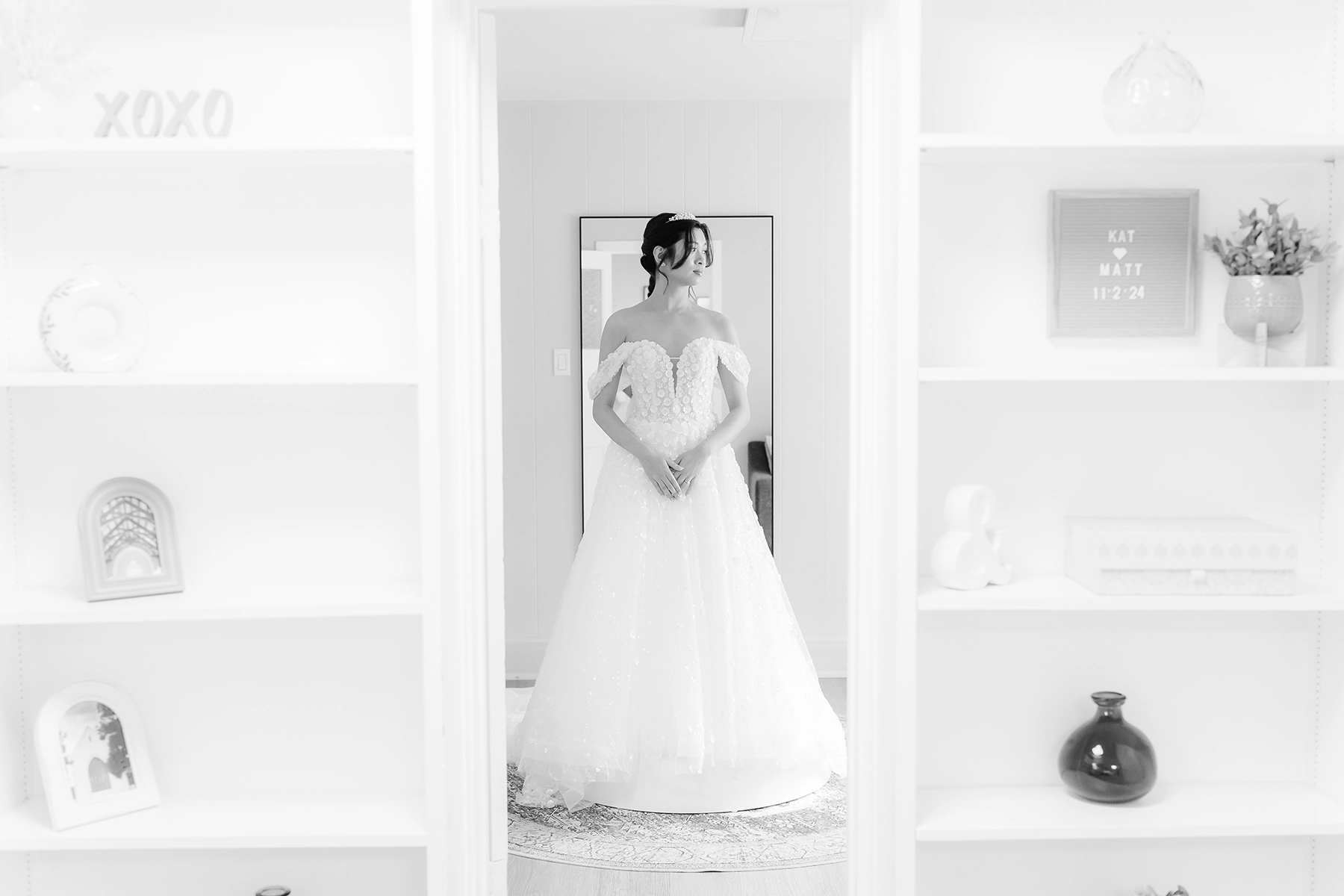Una novia con un elegante vestido sin hombros enmarcada en unas modernas estanterías minimalistas, capturada con una suave estética en blanco y negro, reflejo de las tendencias en auge de la fotografía de bodas de 2025 de narración atemporal de estilo documental y composición íntima.