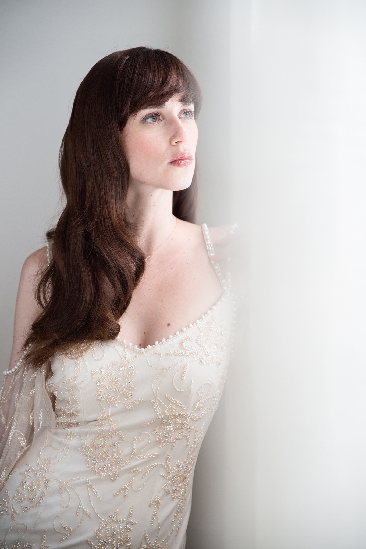 La suave luz de la ventana realza la elegancia natural y resalta los delicados detalles, creando un retrato de novia atemporal.