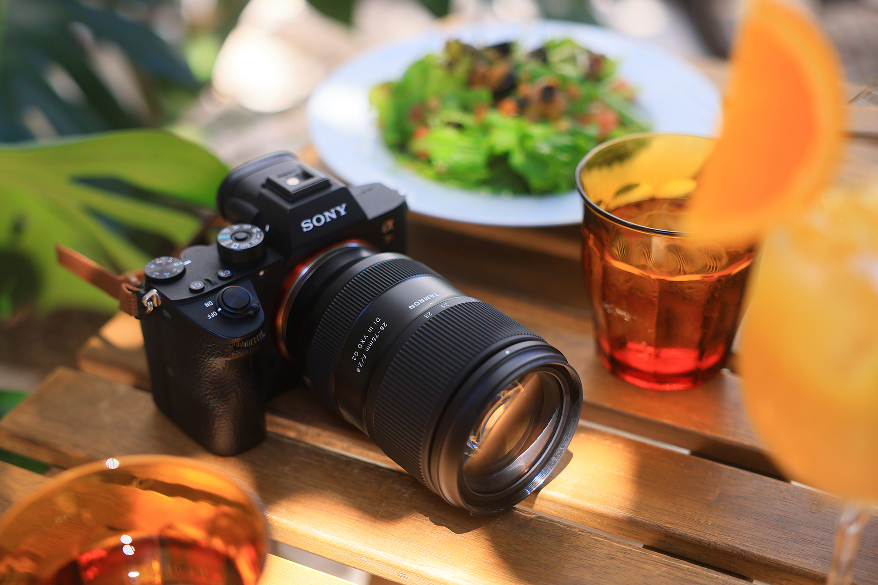 Objetivo Tamron 28-75mm G2 en una cámara sin espejo rodeada de vibrantes bebidas y fresca vegetación, mostrando la creatividad en cada detalle de esta imagen con luz natural.