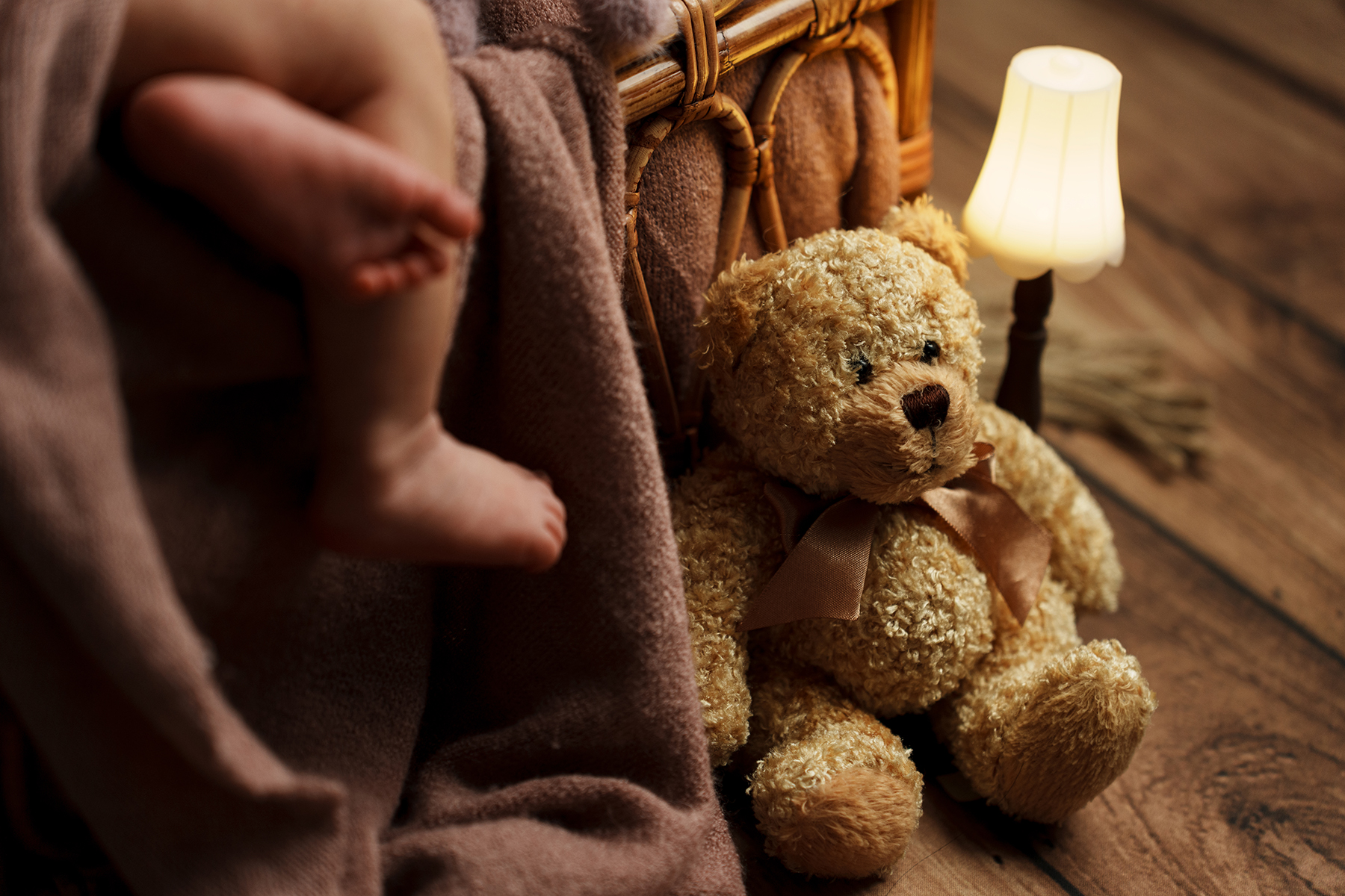 Cálida y acogedora escena nocturna de interior en la que aparece un osito de peluche junto a una cesta de mimbre, suavemente iluminado por una pequeña lámpara sobre un suelo de madera.