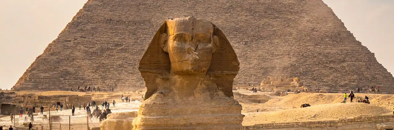 The Great Sphinx of Giza with the Pyramid of Khafre in the background, surrounded by tourists at sunset in Egypt.