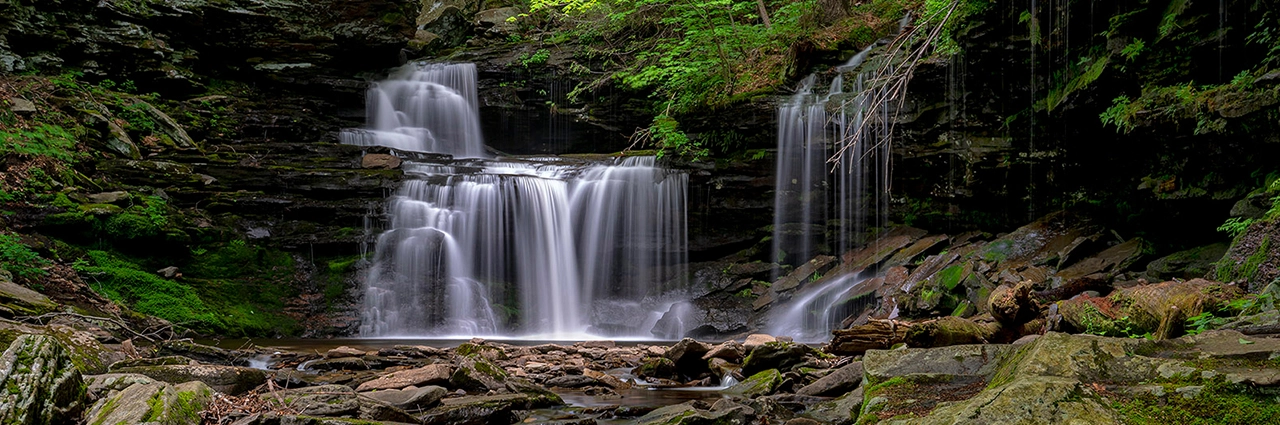 A multi-tiered waterfall flowing gracefully over layers of mossy rock, surrounded by lush greenery and a peaceful forest setting.