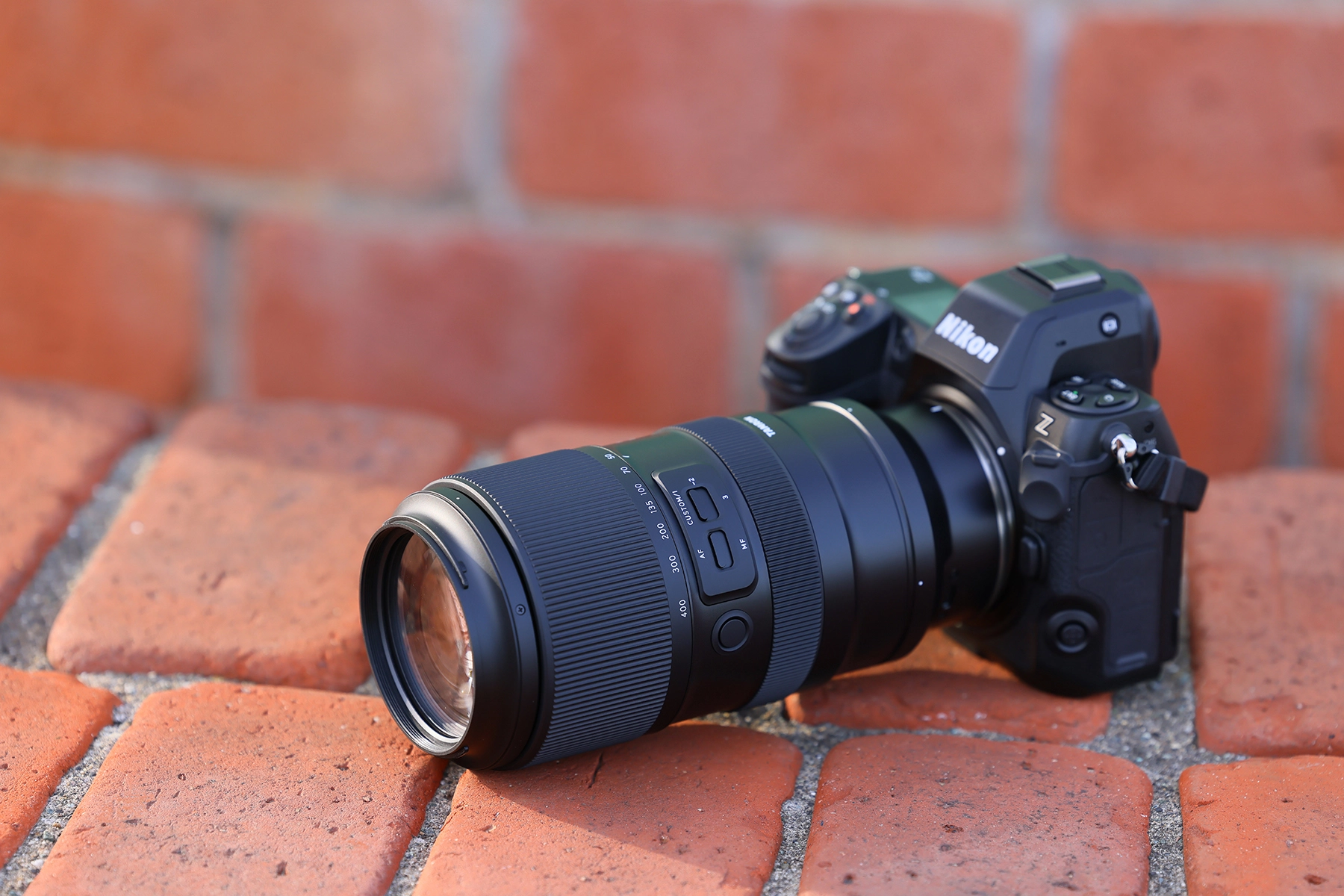Nikon Z series mirrorless camera with TAMRON Z mount 50-400mm telephoto zoom lens resting on brick surface in sunlight.