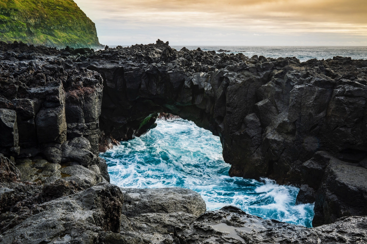 Dramatic rocky sea arch with waves crashing through on a rugged coastline at sunset, shot with a TAMRON Z mount lens at a wide-angle focal length.