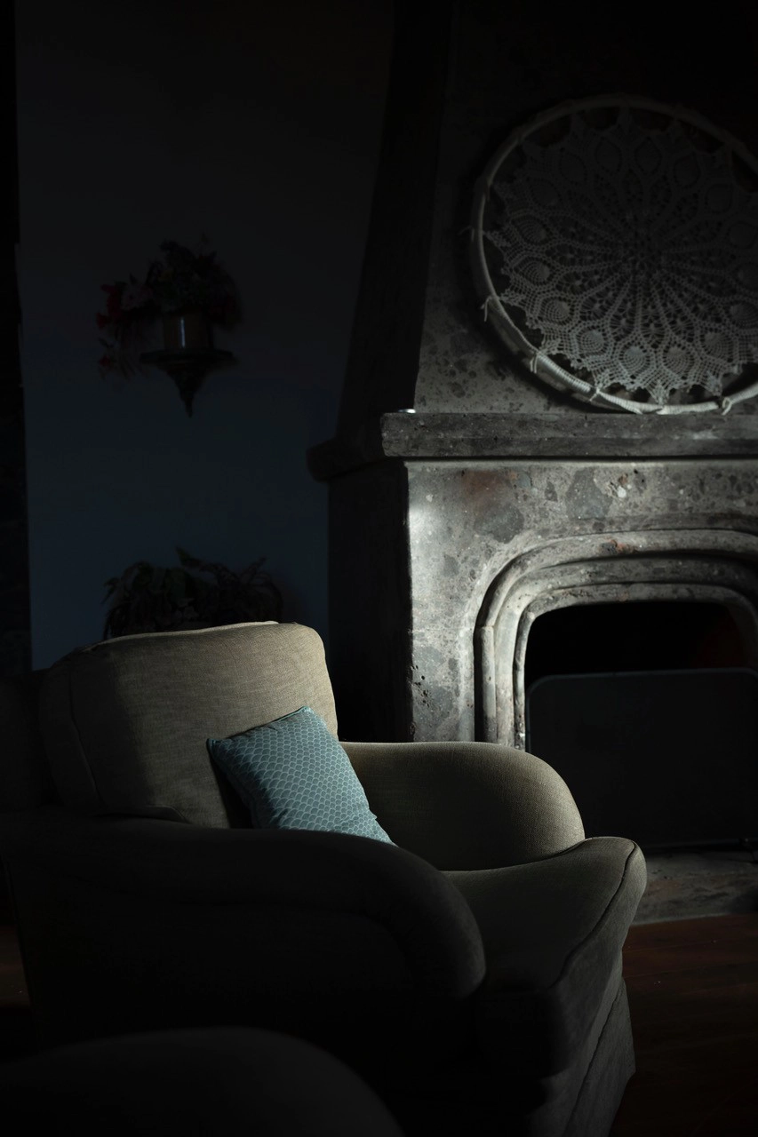 A quiet living room scene with a stone fireplace and soft morning light on an empty armchair&mdash;illustrating the atmospheric setup used when photographing portraits in early morning light.
