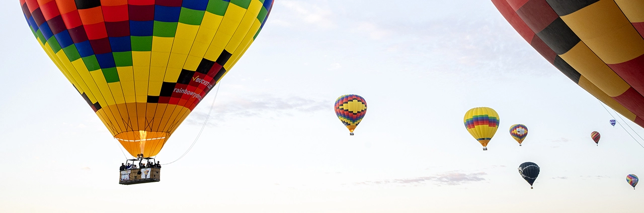 Varios globos aerostáticos de colores flotando en un cielo despejado durante un festival de globos, con un gran y vibrante globo que transporta pasajeros en primer plano.