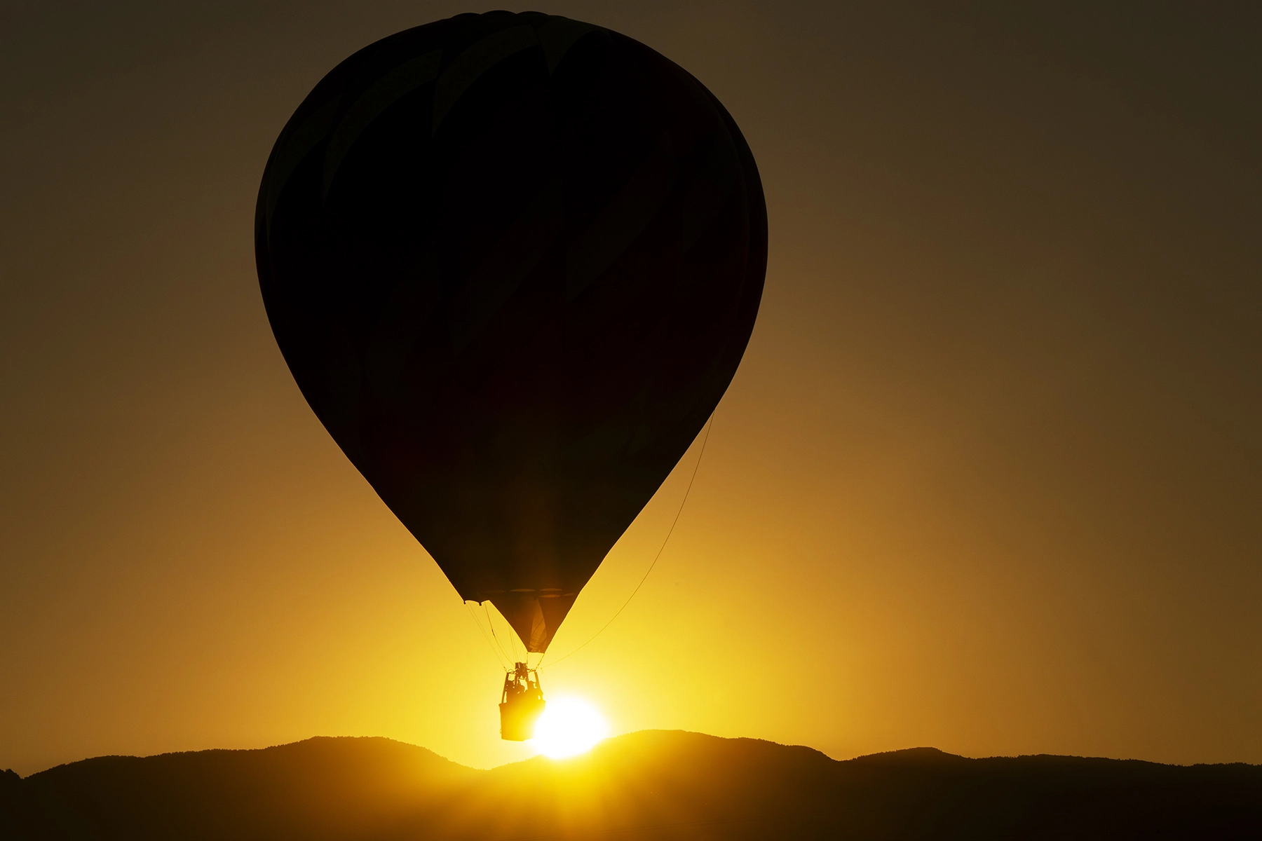 Silueta de un globo aerostático flotando sobre los picos de las montañas en un cielo dorado al amanecer.