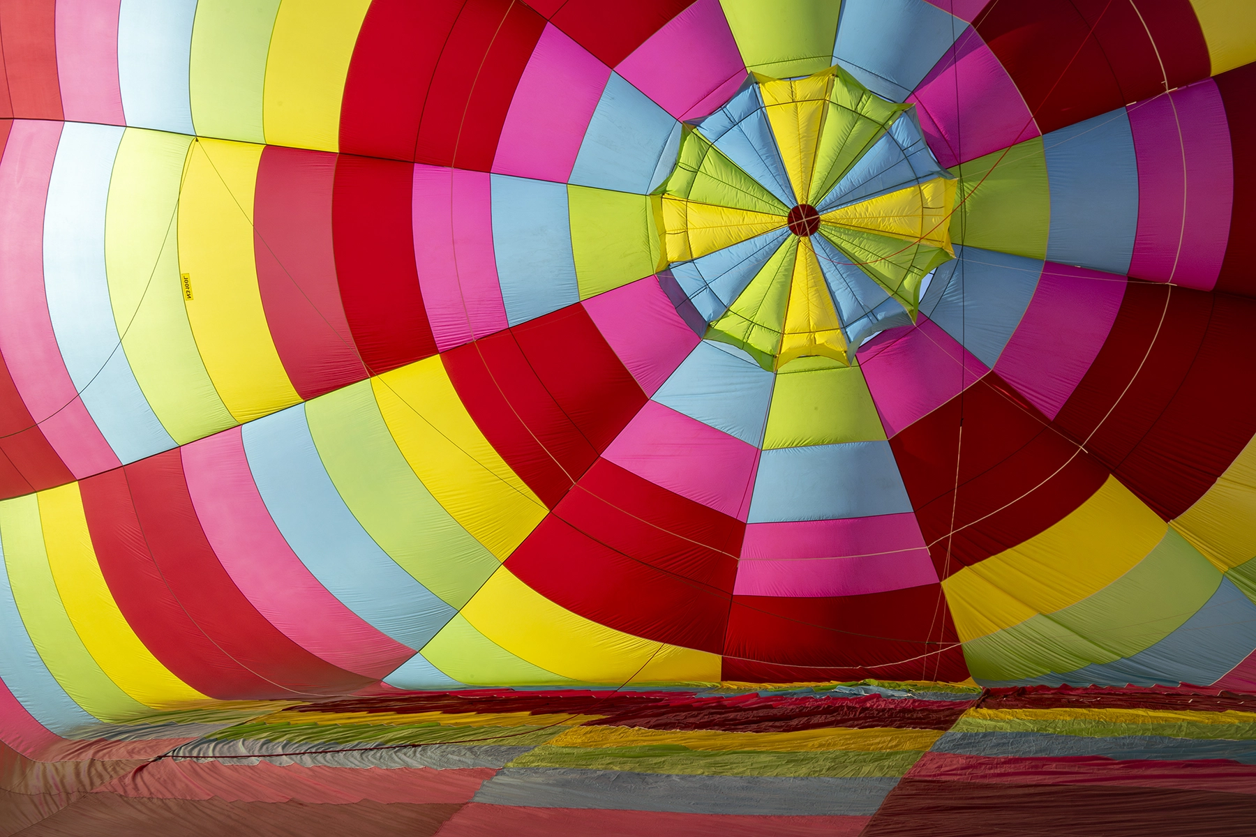 Vibrante vista interior de un globo aerostático parcialmente inflado, que muestra coloridos paneles de tela en rojo, amarillo, azul, verde y rosa.
