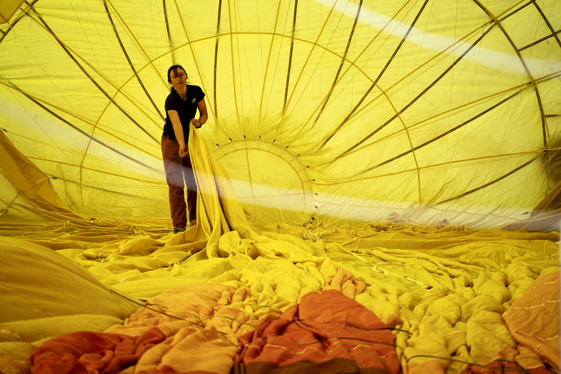 Persona dentro de un globo aerostático amarillo parcialmente inflado, ajustando la tela durante el proceso de preparación en un festival de globos.
