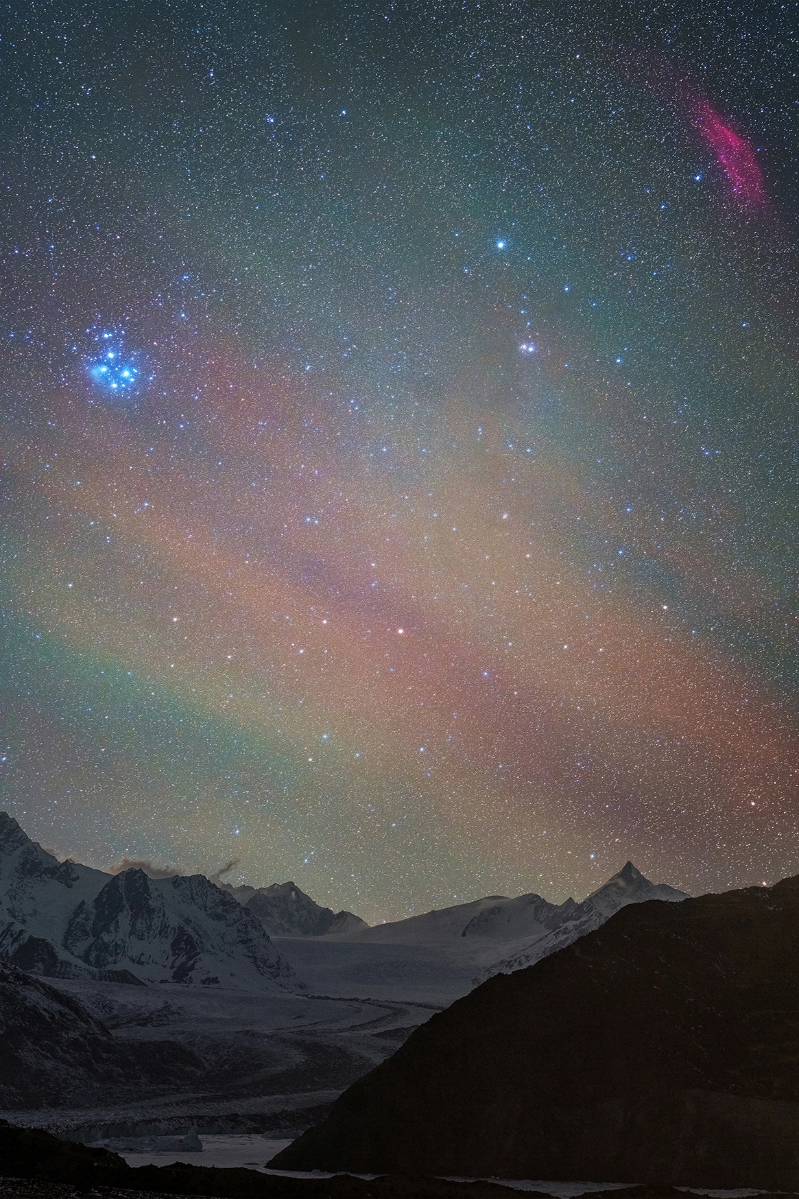 The Pleiades and California Nebula glow above glacier peaks, with colorful airglow layers captured in vivid detail through astrophotography with a macro lens.