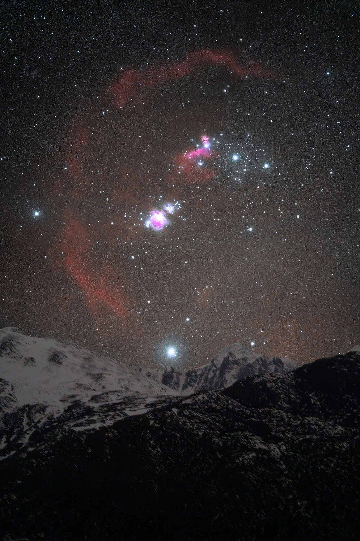 Orion rises above snow-covered peaks, with the Barnard Loop and surrounding nebulae vividly captured through astrophotography with a macro lens.