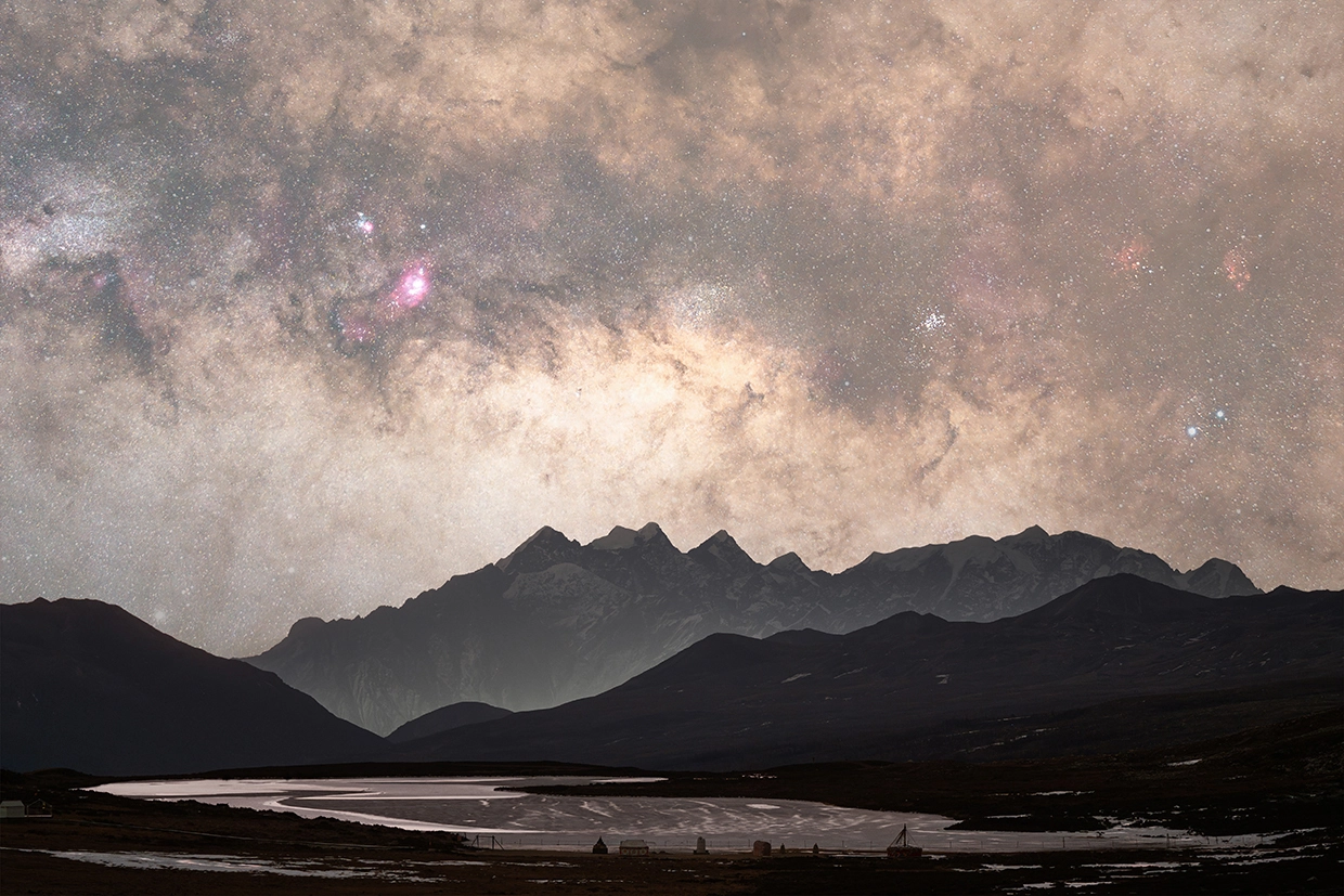 The Milky Way's galactic core rises above snow-capped peaks and a reflective lake, captured in rich texture through astrophotography with a macro lens.