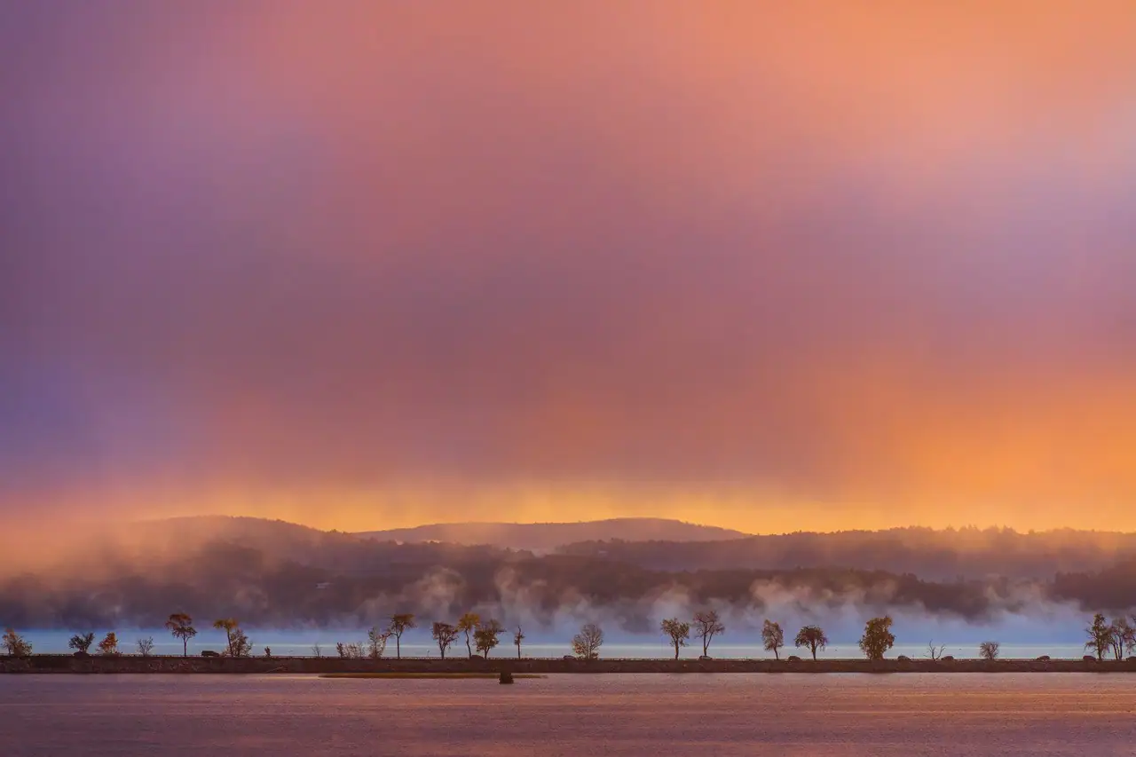 A tranquil lake at sunrise, with mist rising over the water and a colorful sky reflecting on the landscape.