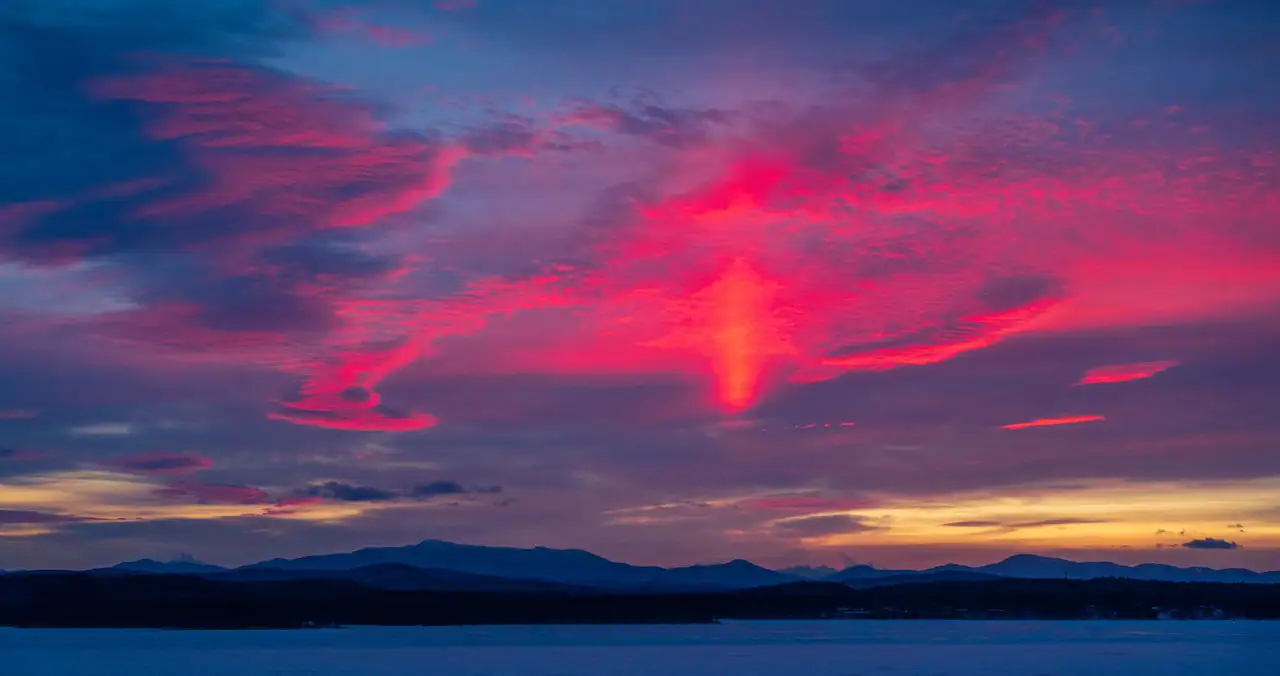 A vibrant sunset paints the sky in shades of pink and purple over a mountain landscape and a frozen lake.