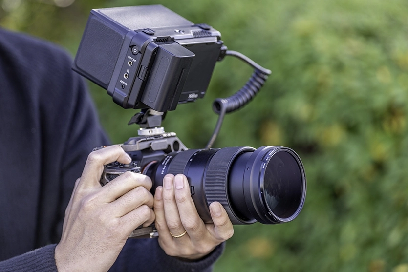 A videographer demonstrates the basics of camerawork for video shooting using a mirrorless camera equipped with a Tamron lens and external monitor.