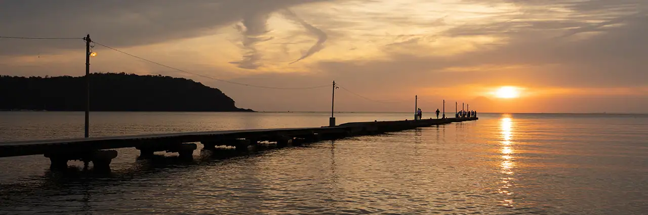 Coucher de soleil à l'heure dorée sur une mer calme avec des silhouettes sur une jetée, capturé lors de l'examen du Tamron 16-30mm F2.8 G2 - mettant en évidence le contraste dynamique et la clarté d'un bord à l'autre au grand angle.