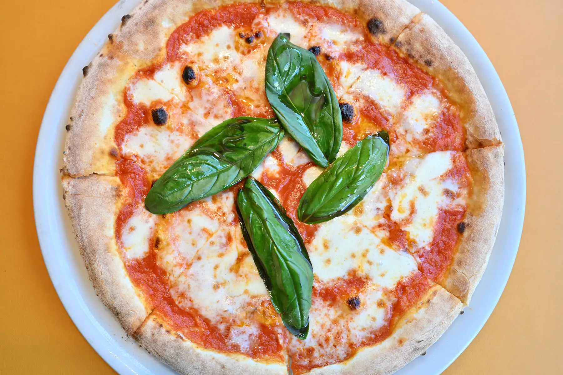 Photo aérienne d'une pizza Margherita avec des feuilles de basilic frais, capturée à 30 mm lors de l'examen du Tamron 16-30 mm F2.8 G2 - mettant en valeur la texture nette et les couleurs vives dans la photographie alimentaire en gros plan.