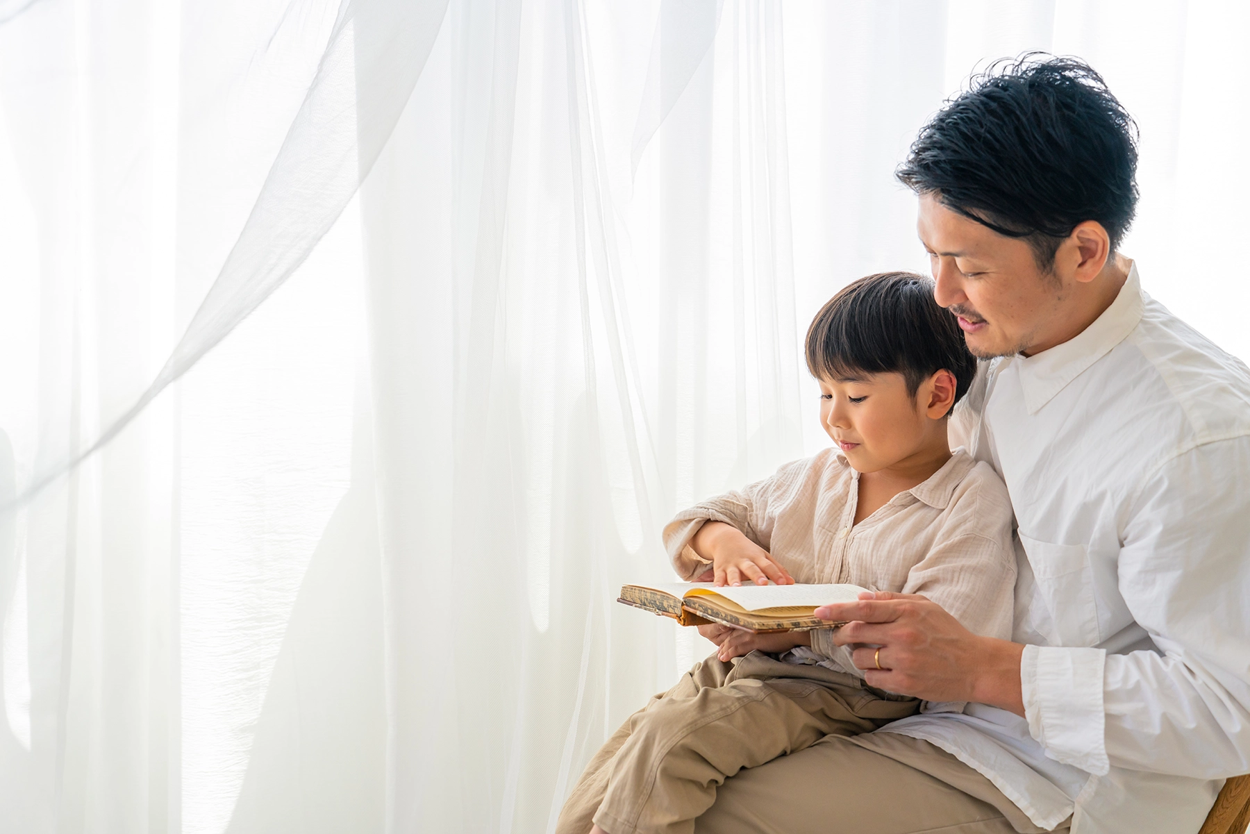 Father and son reading together in soft natural light, captured with a standard lens to create a natural angle of view and intimate atmosphere.