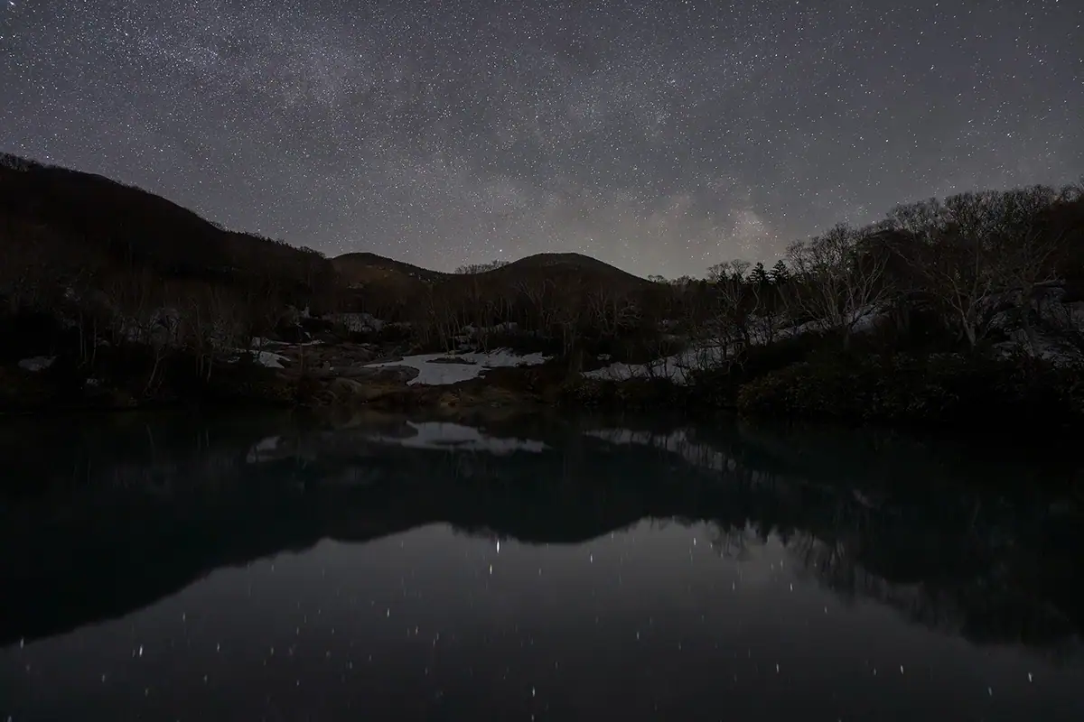Paisagem noturna com céu estrelado e reflexo de montanha capturada usando o Astro Focus Lock para astrofotografia com o TAMRON Lens Utility™.