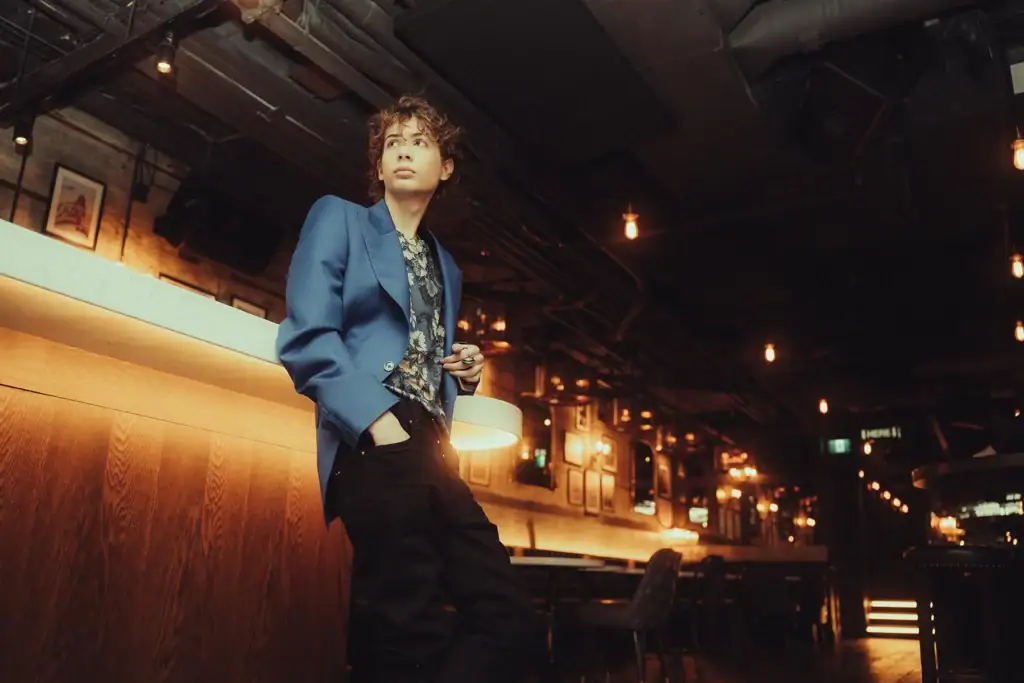 Um jovem ator em um restaurante mal iluminado, encostado em um bar.