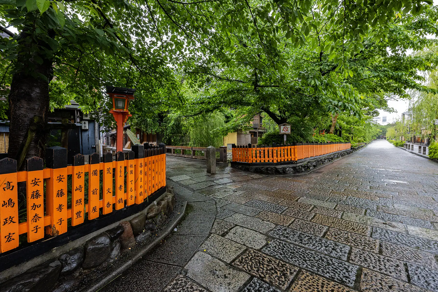 A stone walkway with black and orange fencing and green trees