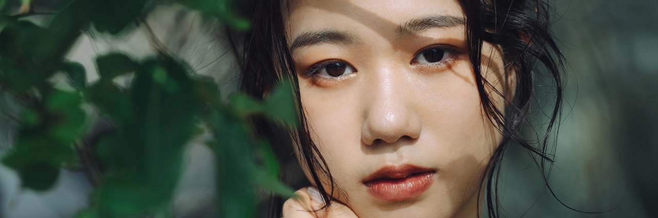 Portrait en gros plan d'une femme avec un premier plan vert flou, capturé à l'aide d'une longueur focale de téléobjectif pour créer un bokeh doux et une compression de l'arrière-plan.