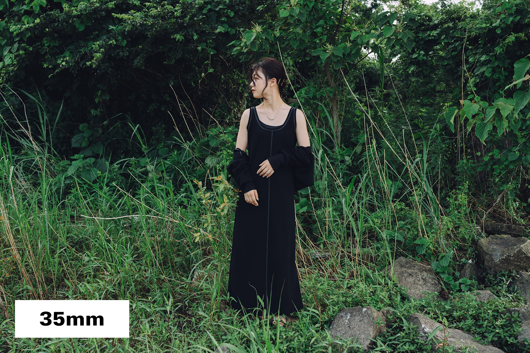 Portrait en pied d'une femme debout dans la verdure, photographiée à la focale de 35 mm pour inclure le contexte environnemental et les détails de l'arrière-plan.