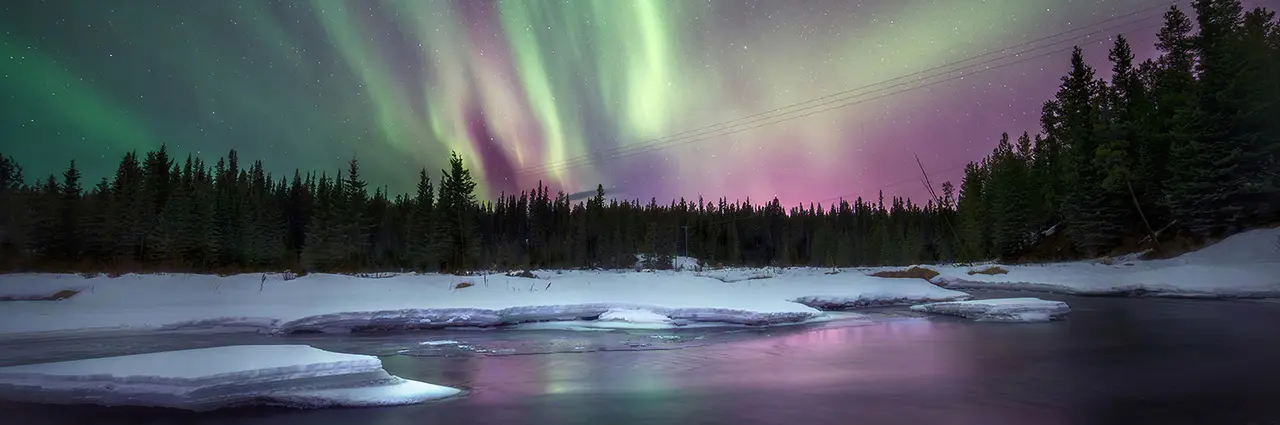 Northern Lights dance above a snow-covered river in the Yukon, captured during a Tamron 16-30mm field test by photographer Yoshiki Fujiwara, showcasing the lens’s ultra-wide perspective and low-light performance.