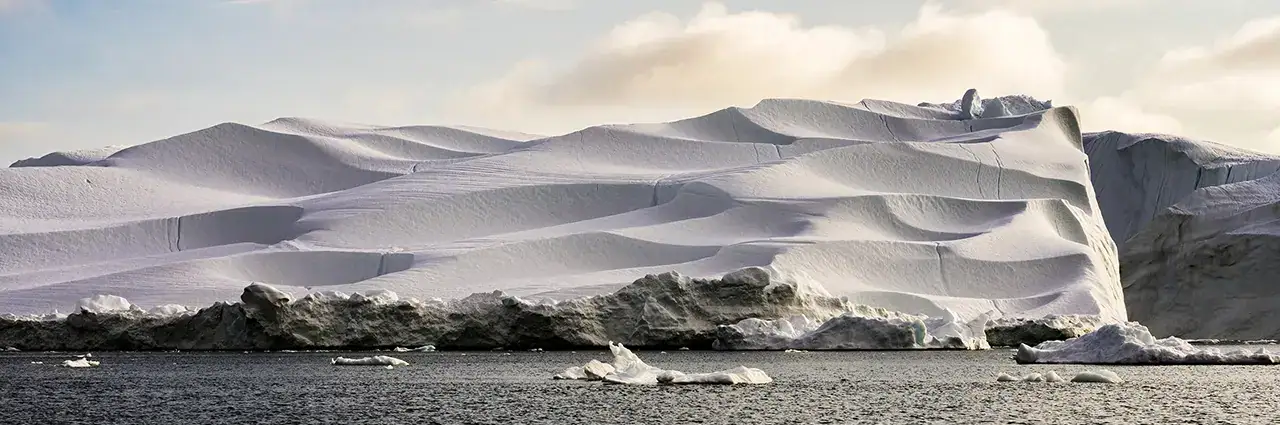 Panoramique d'un iceberg dans la baie de Disko, au Groenland, photographié avec l'objectif Tamron 28-75mm G2, mettant en valeur les motifs sculptés de la glace et la lumière arctique.