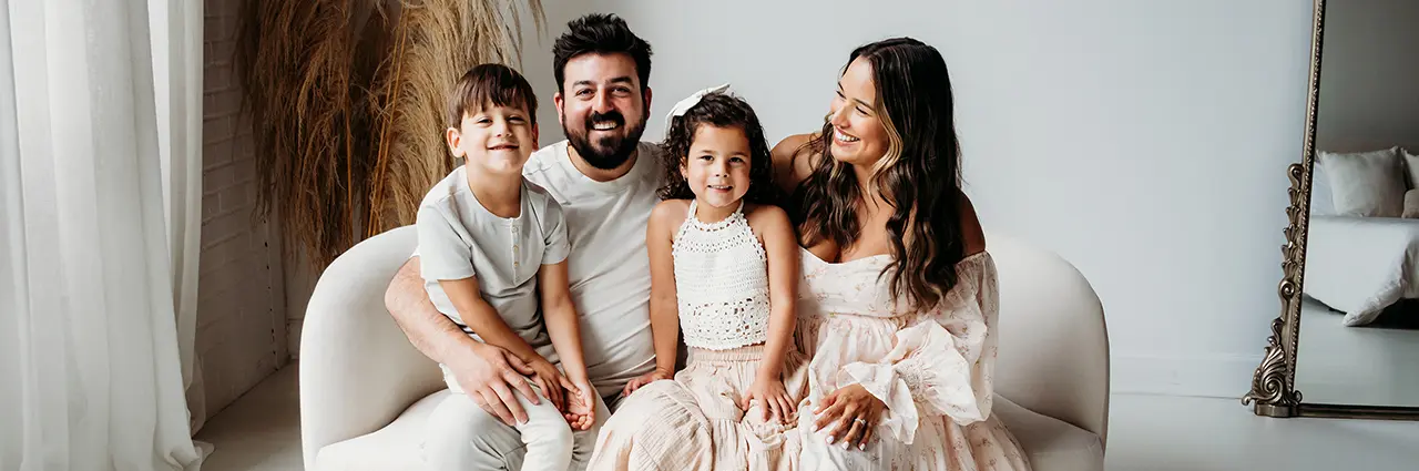 Famille assise sur un canapé blanc, souriant pendant une séance photo - exemple de l'objectif principal par rapport à l'objectif zoom pour la photographie de famille.