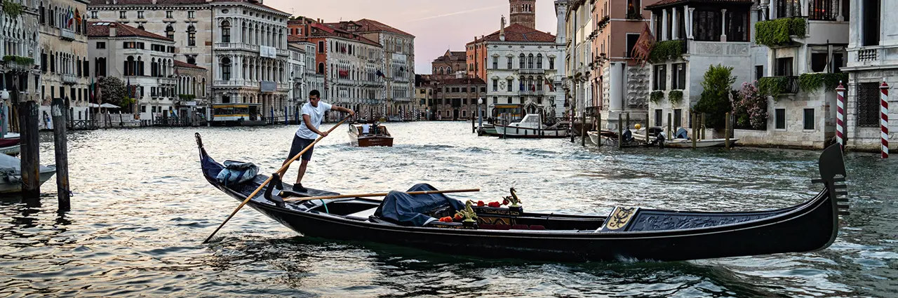 A gondolier rows along the Grand Canal at sunset, showcasing the atmosphere of Italy’s Floating City for this Venice travel photography guide.