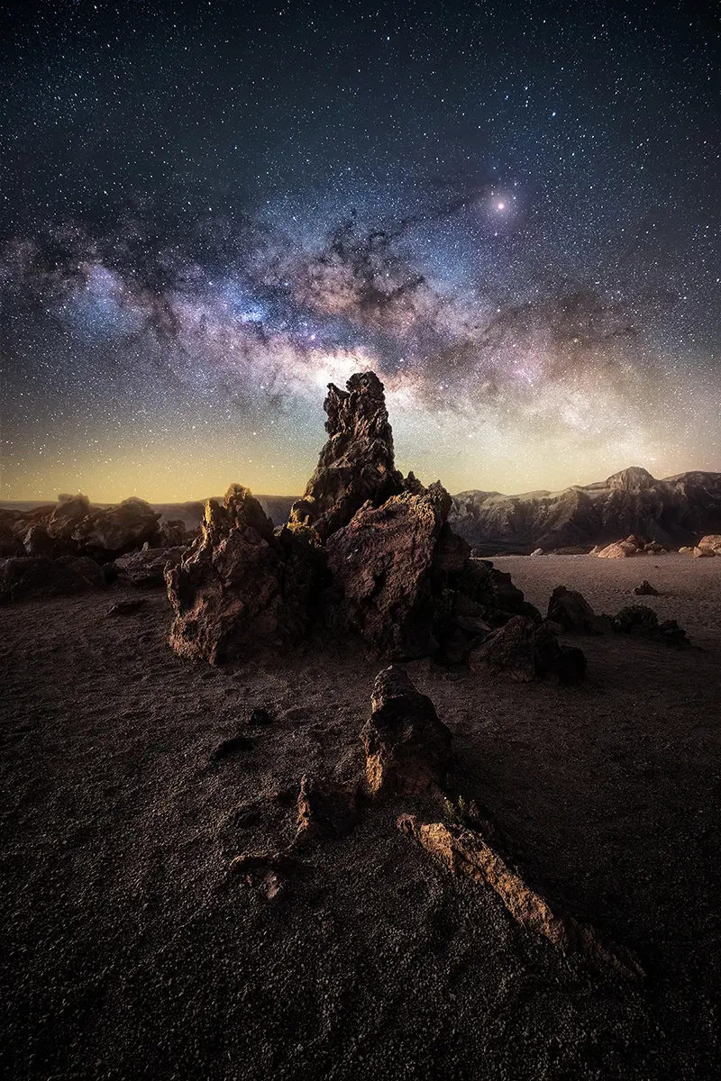 Towering rock formation illuminated under the Milky Way, photographed with a fast Tamron f/2.8 lens &mdash; an example of the brightness and clarity from the best lens for astrophotography.