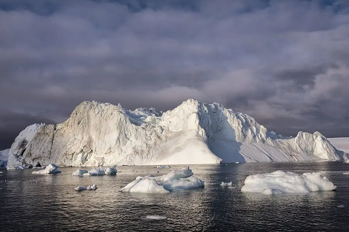 Iceberg massif dans la baie de Disko, au Groenland, photographié avec l'objectif Tamron sous un ciel arctique dramatique et une douce lumière du soir.