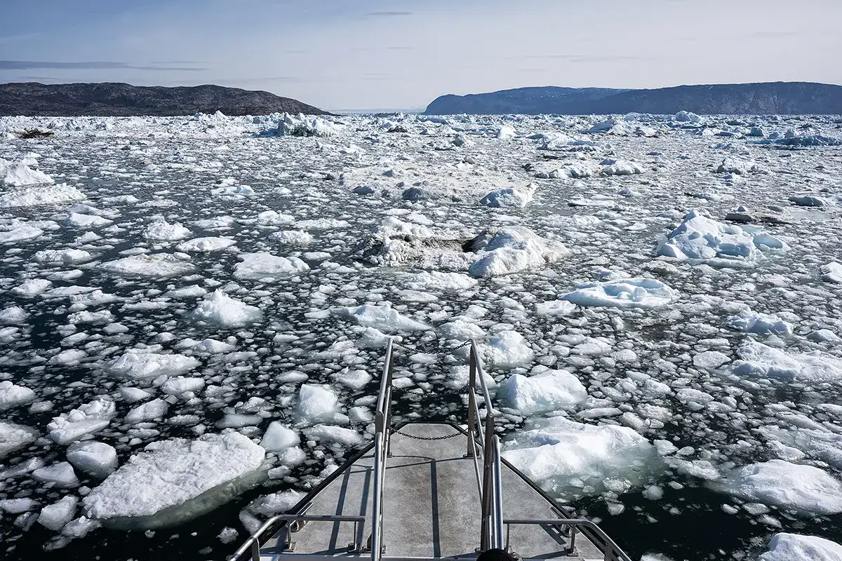 Vue d'un bateau naviguant sur la glace de mer dans la baie de Disko, au Groenland, photographiée avec un objectif Tamron grand angle G2 pour capturer les textures de l'Arctique et le paysage marin gelé.