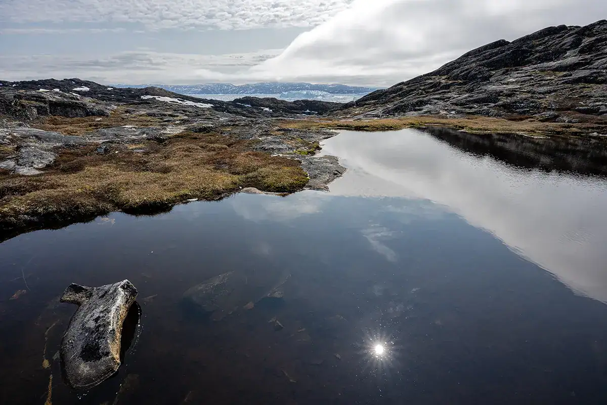 Paysage de toundra arctique près d'Ilulissat, au Groenland, avec un bassin d'eau réfléchissant et un terrain rocheux, capturé avec un objectif grand angle Tamron.