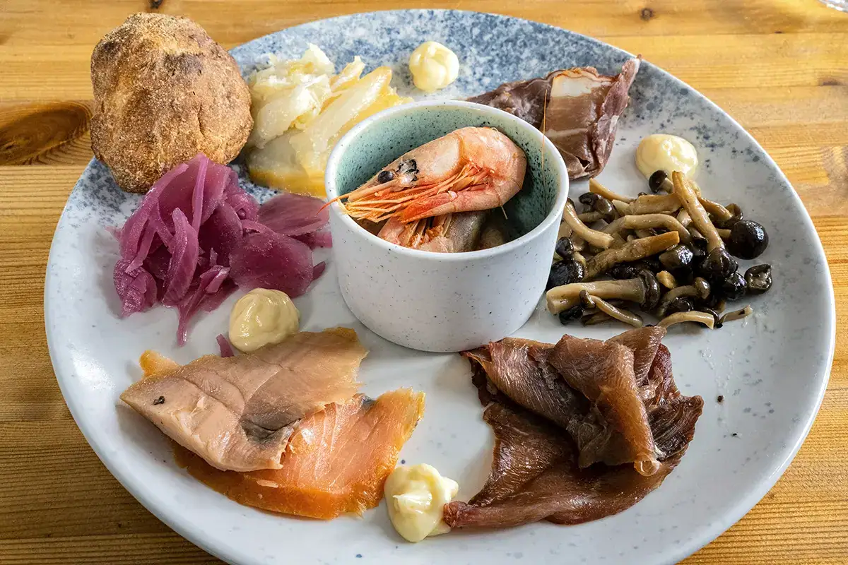 Plateau traditionnel groenlandais composé de saumon fumé, de crevettes, d'oignons marinés, de poisson séché et de spécialités locales, photographié avec un objectif Tamron.