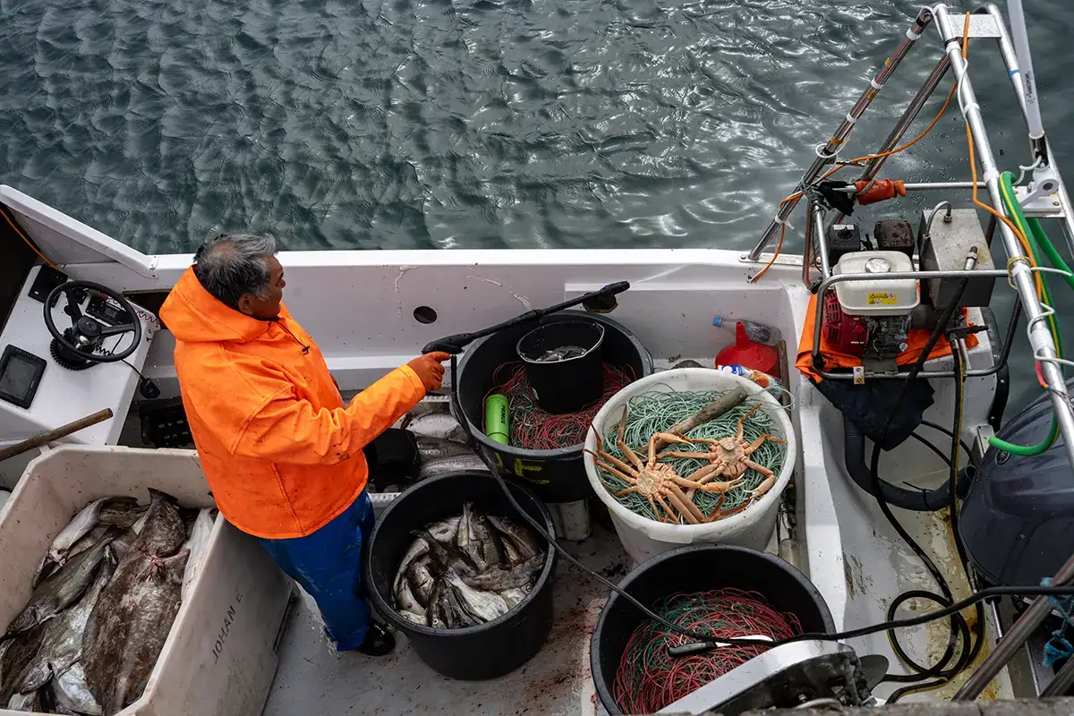 Pêcheur groenlandais en veste orange vif sur un bateau avec des poissons, des crabes et des filets fraîchement pêchés, photographié avec un objectif Tamron dans la baie de Disko.