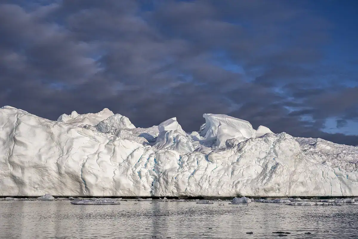 Iceberg imposant dans la baie de Disko, au Groenland, avec des fissures bleues et des textures mises en évidence par la lumière arctique, photographié avec un téléobjectif Tamron.