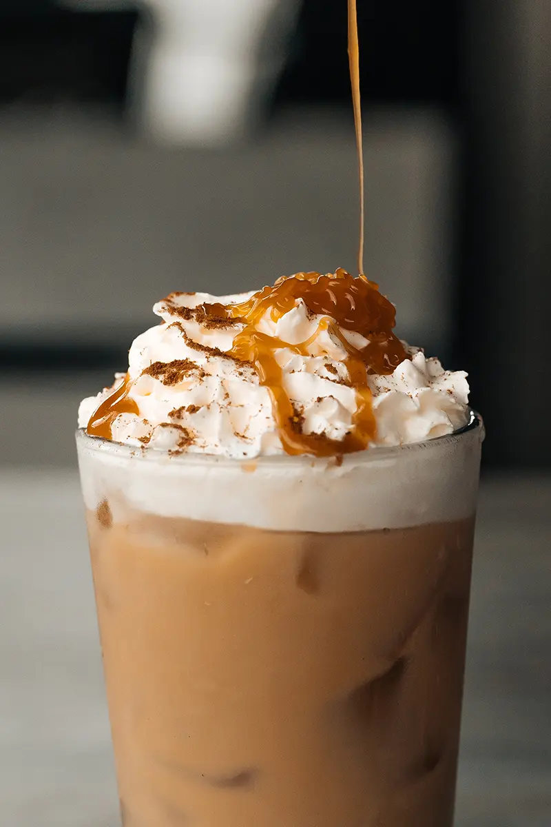 Café com leite gelado de outono, coberto com chantilly, canela e gotas de caramelo, com estilo para fotografia de alimentos e bebidas de outono.