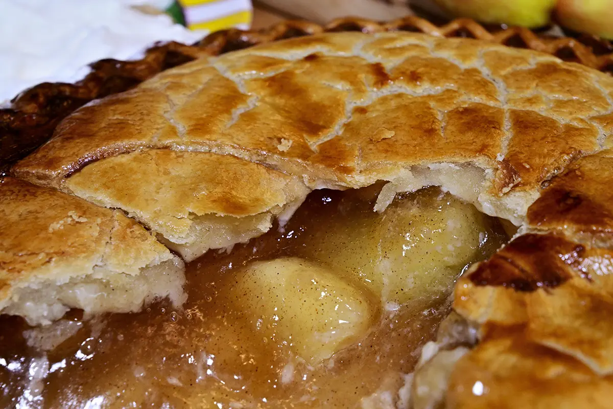 Close-up de uma torta de maçã dourada com uma crosta escamosa e recheio quente de maçã com especiarias e canela.