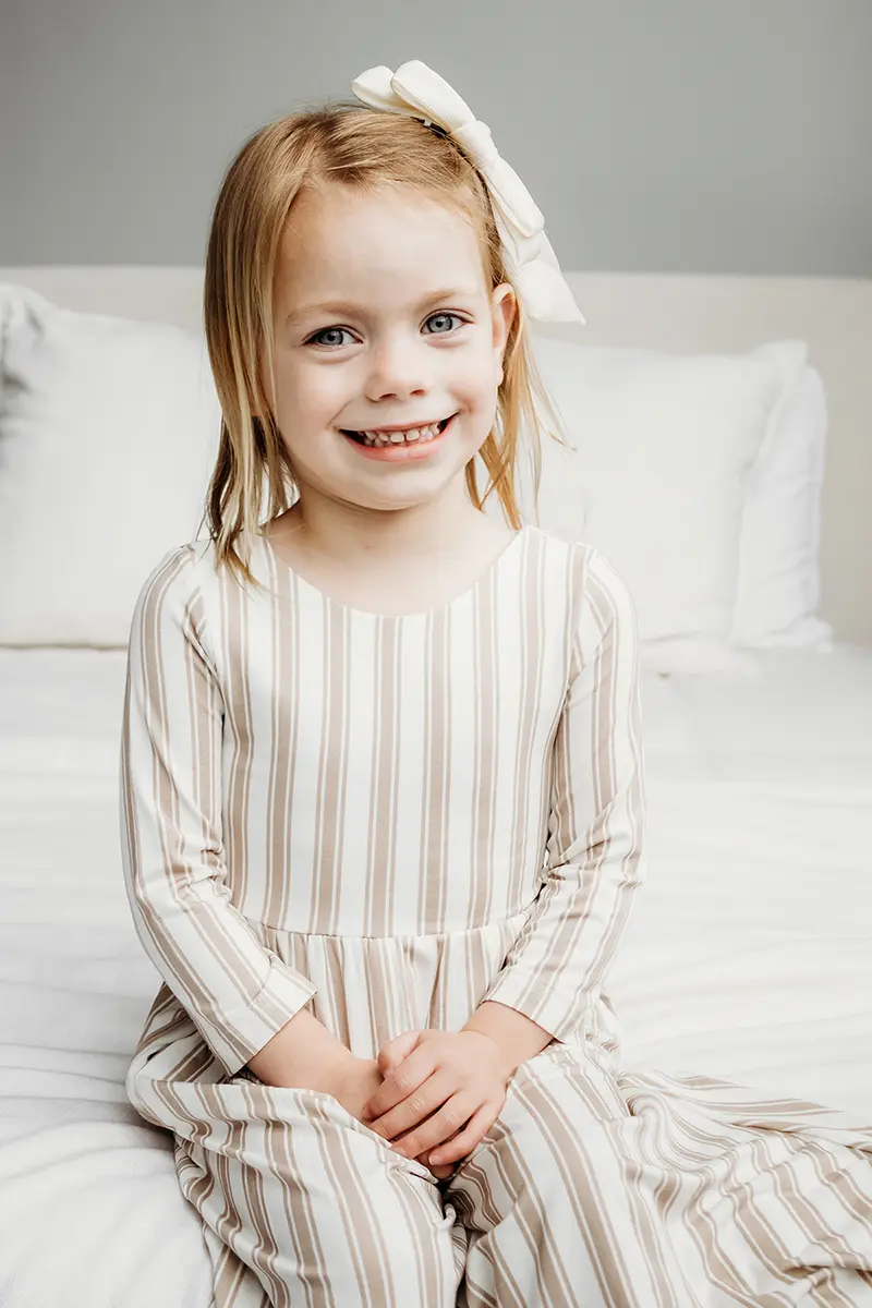Jeune fille en robe rayée souriant lors d'une séance de portrait, montrant un exemple d'objectif principal par rapport à un objectif zoom pour la photographie de famille.