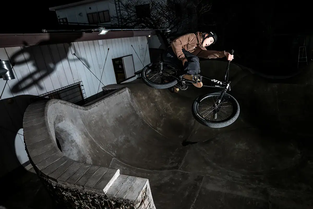 Urban sports photography of BMX rider performing trick at night in a concrete skatepark bowl