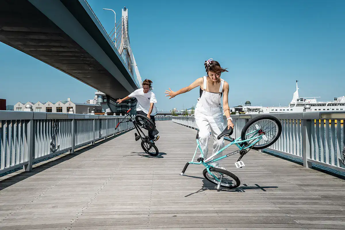 BMX riders performing flatland tricks on boardwalk beneath Aomori bridge. Captured during an urban sports photography shoot.