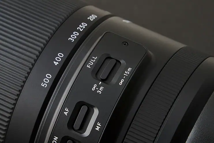 Close-up of a TAMRON telephoto lens showing focus limiter and AF/MF switch controls with detailed focal length markings.