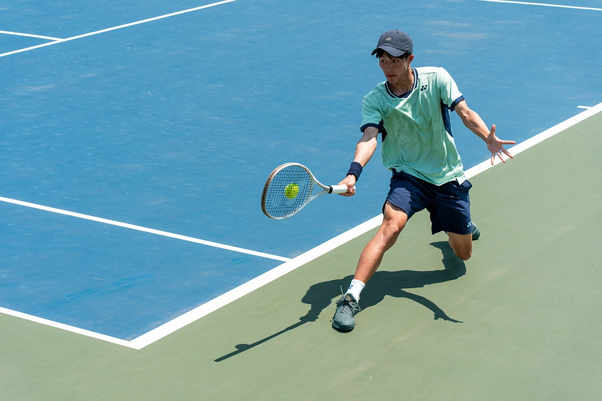 A man playing tennis on a green and blue tennis court.